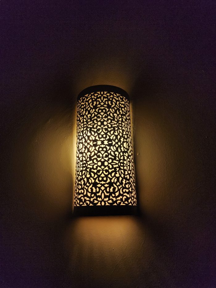 Handmade filigree brass wall sconce with intricate floral cutout pattern and warm ambient wall lighting.