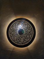 Handmade round brass wall light with floral rosette openwork, solid center medallion and warm glowing halo.