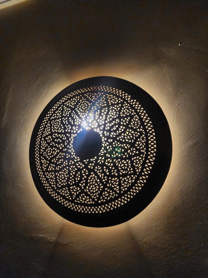 Handmade round brass wall light with floral rosette openwork, solid center medallion and warm glowing halo.