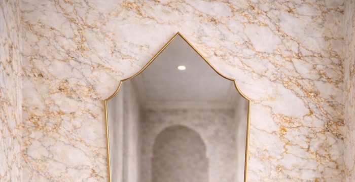 Handmade Moroccan pointed arch brass mirror with slim gold frame above a bathroom vanity.