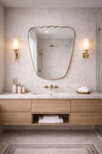 Handmade wavy top brass wall mirror with tapered sides and solid brass frame displayed above bedroom console.