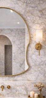 Arched freeform brass wall mirror with solid brass frame and clear glass above a bathroom vanity.