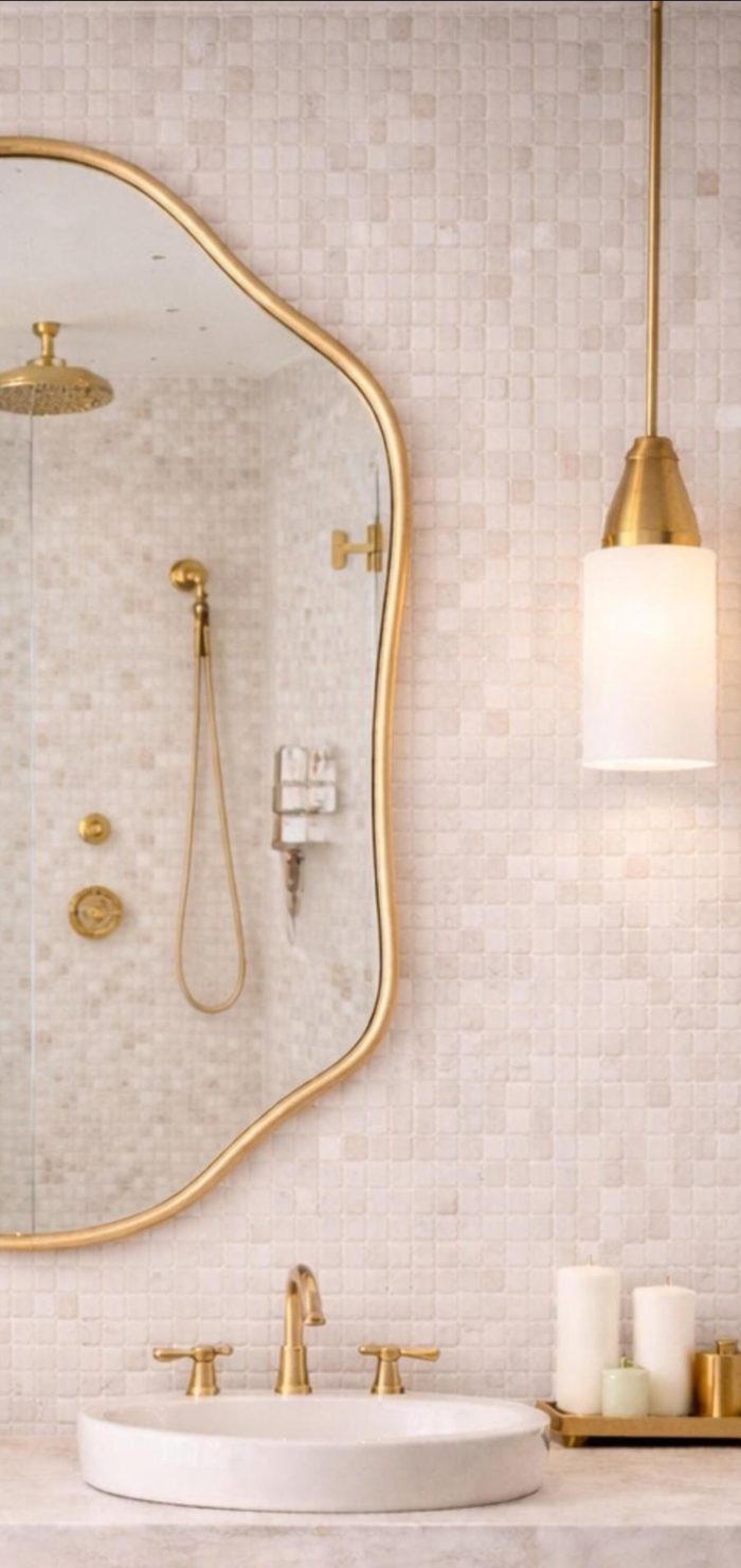 Handmade sculpted oval brass wall mirror with flowing curved edges and solid brass frame above double bathroom vanity.