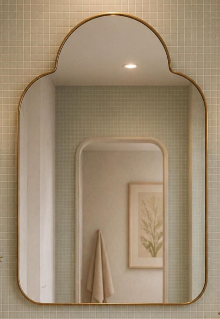 Handmade rounded crown brass wall mirror with clear glass and solid brass frame displayed above an elegant bathroom vanity.
