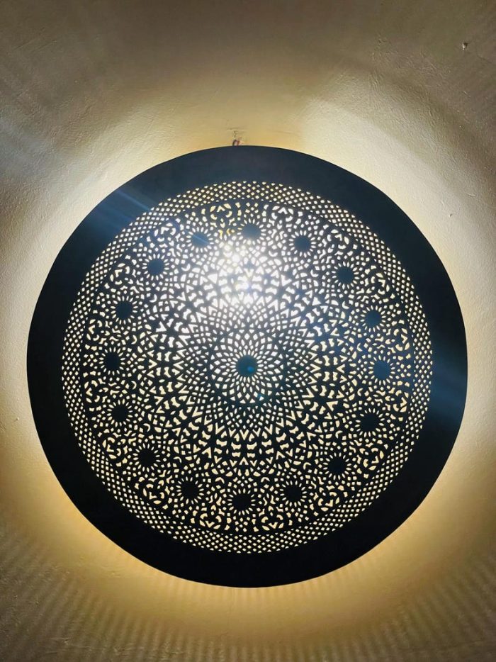 Handmade round brass wall light with intricate mandala pattern and radiant warm halo illumination.