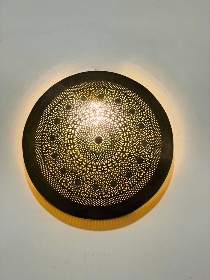Handmade round brass wall light with intricate mandala pattern and radiant warm halo illumination.