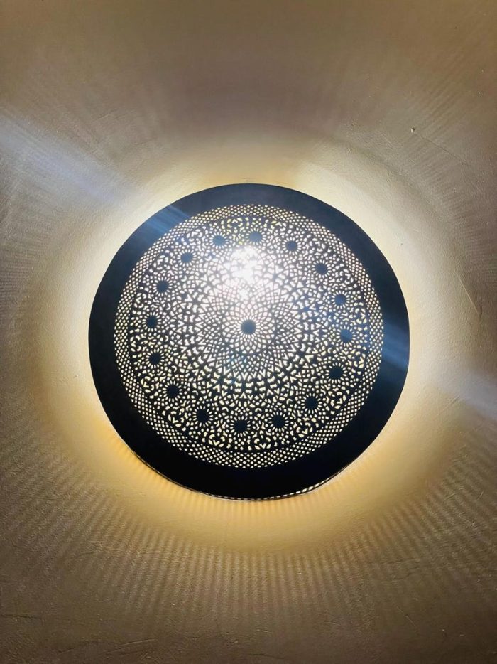 Handmade round brass wall light with intricate mandala pattern and radiant warm halo illumination.