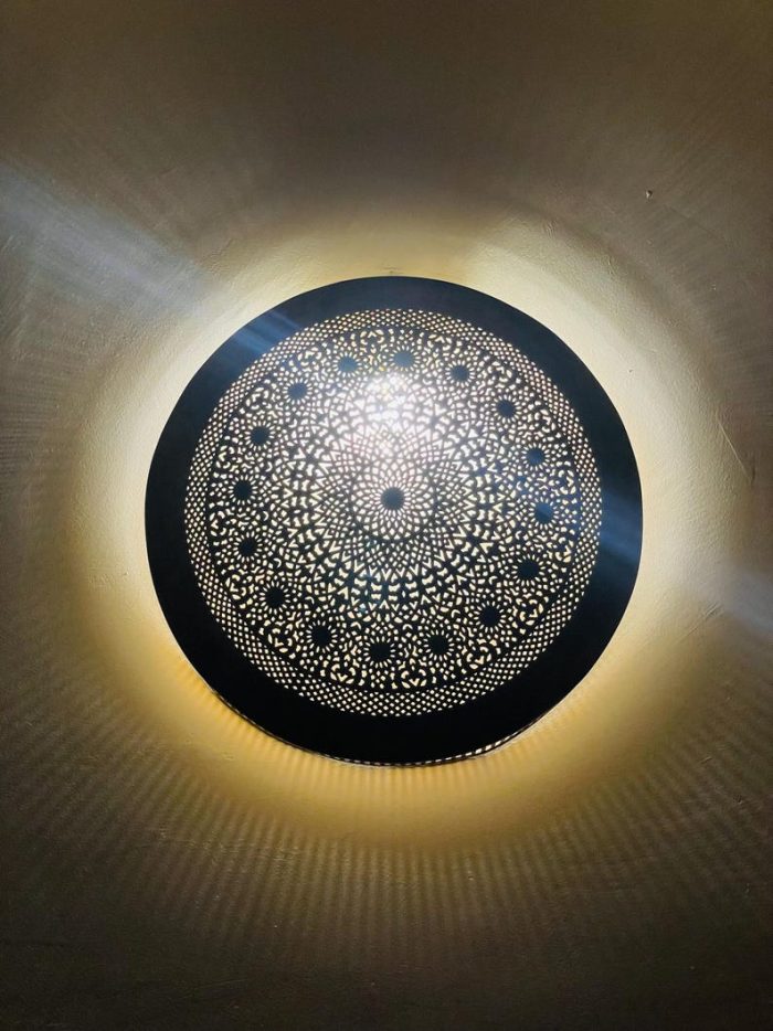 Handmade round brass wall light with intricate mandala pattern and radiant warm halo illumination.