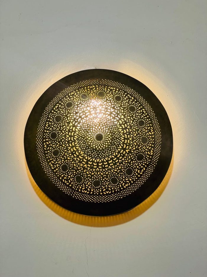 Handmade round brass wall light with intricate mandala pattern and radiant warm halo illumination.