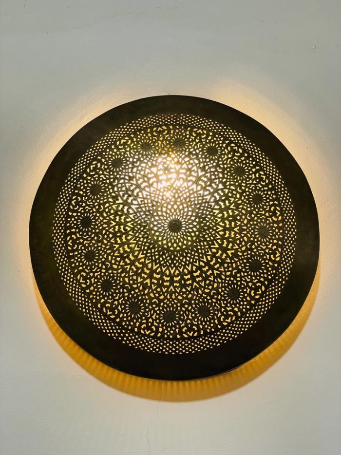 Handmade round brass wall light with intricate mandala pattern and radiant warm halo illumination.