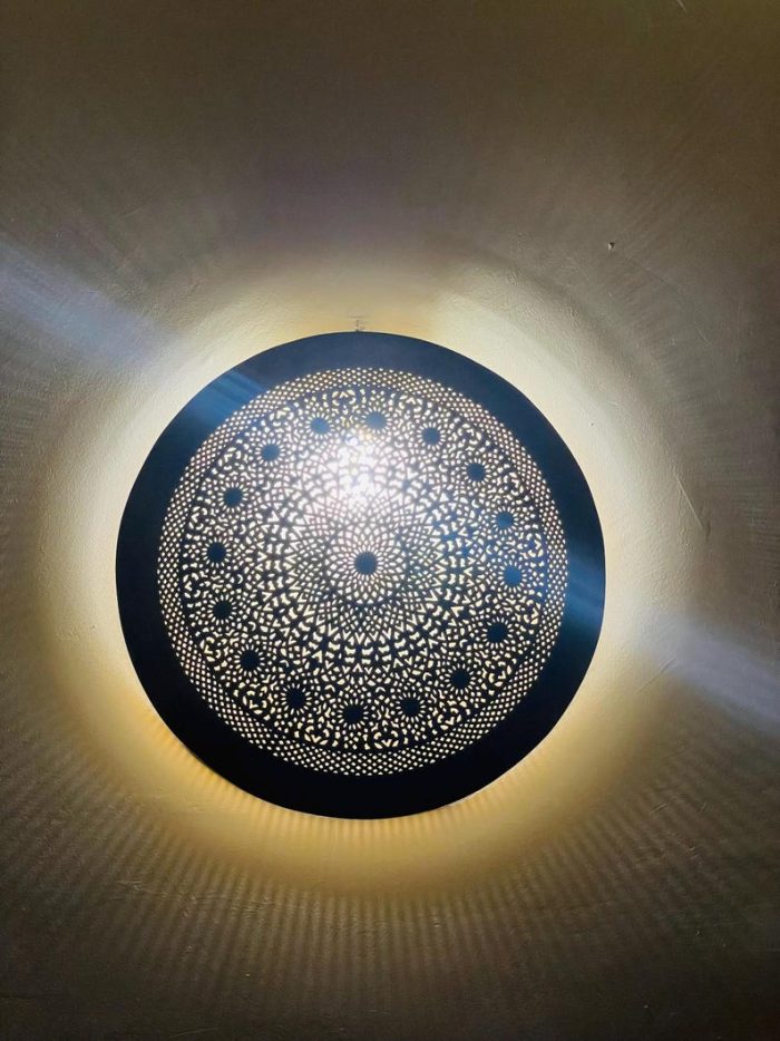 Handmade round brass wall light with intricate mandala pattern and radiant warm halo illumination.