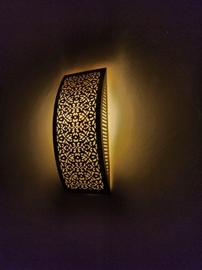 Handmade lattice filigree brass wall sconce with bowed rectangular shape, ornamental openwork and warm ambient lighting.