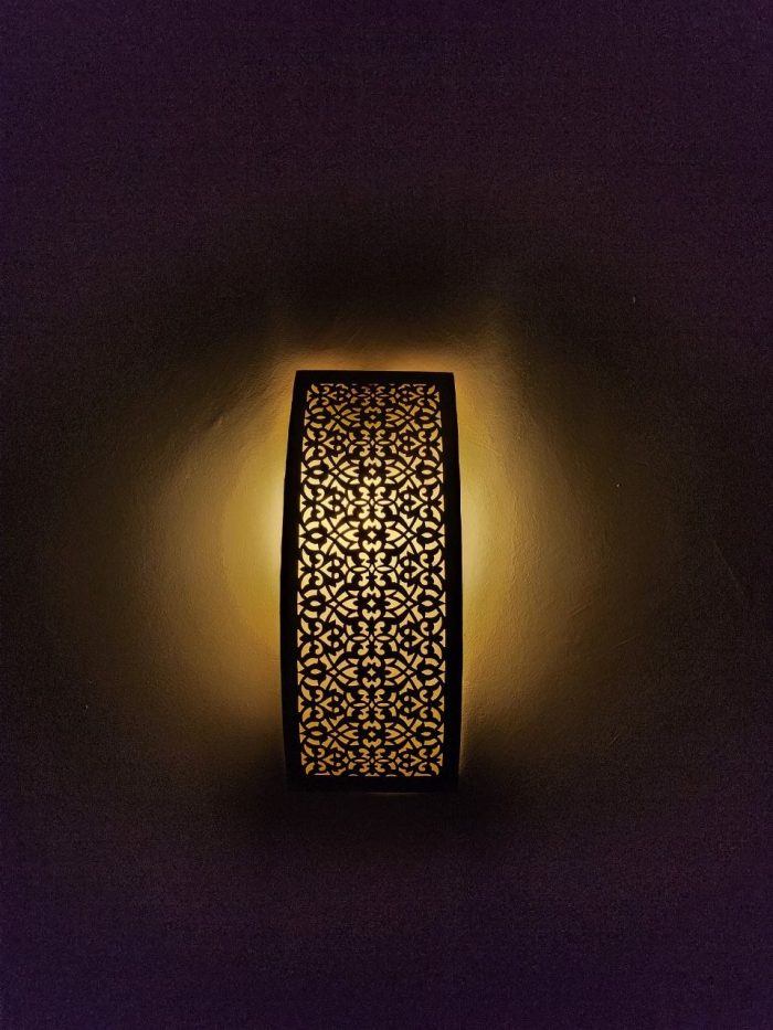 Handmade lattice filigree brass wall sconce with bowed rectangular shape, ornamental openwork and warm ambient lighting.
