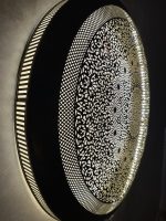 Handmade Moroccan brass wall light with round pierced floral design and warm halo illumination.
