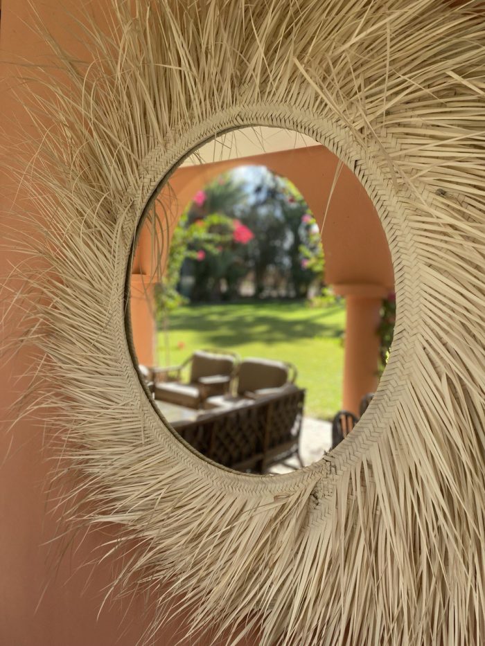Handwoven palm leaf mirror with round glass center and natural sunburst fringe wall decor