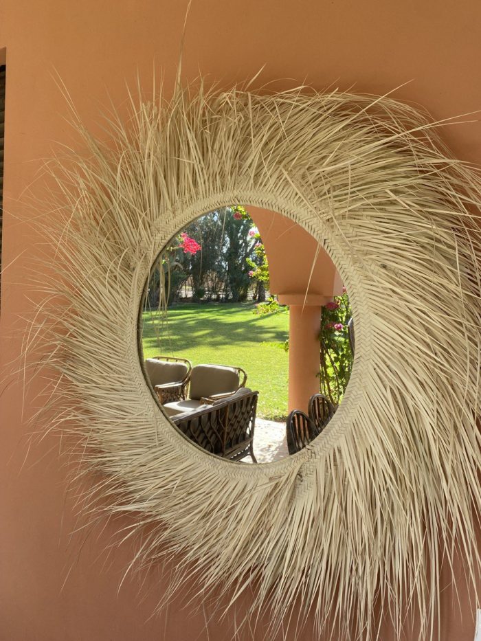 Handwoven palm leaf mirror with round glass center and natural sunburst fringe wall decor