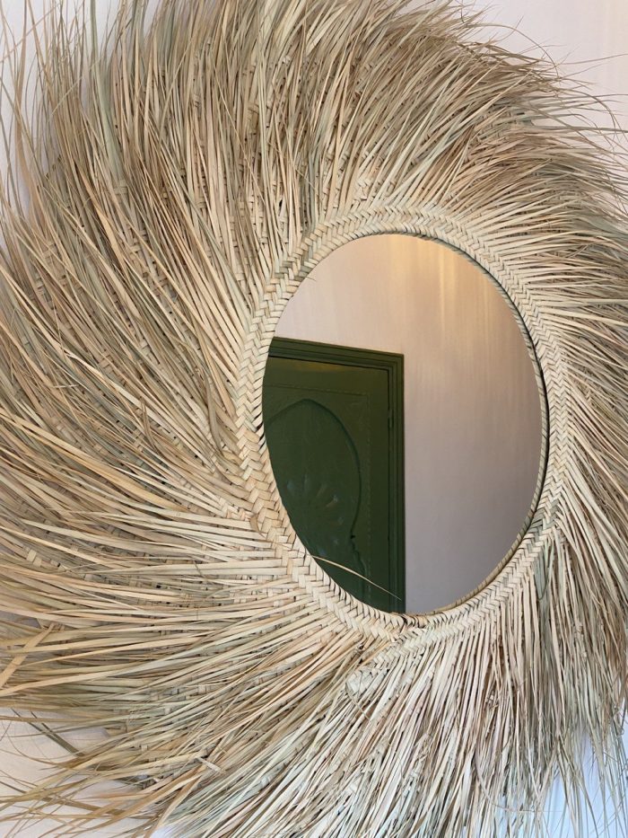 Handwoven palm leaf mirror with round glass center and natural sunburst fringe wall decor
