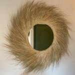 Handwoven palm leaf mirror with round glass center and natural sunburst fringe wall decor