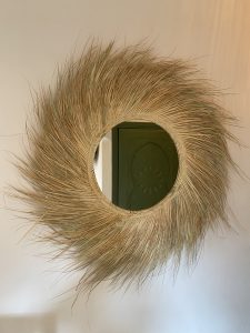 Handwoven palm leaf mirror with round glass center and natural sunburst fringe wall decor