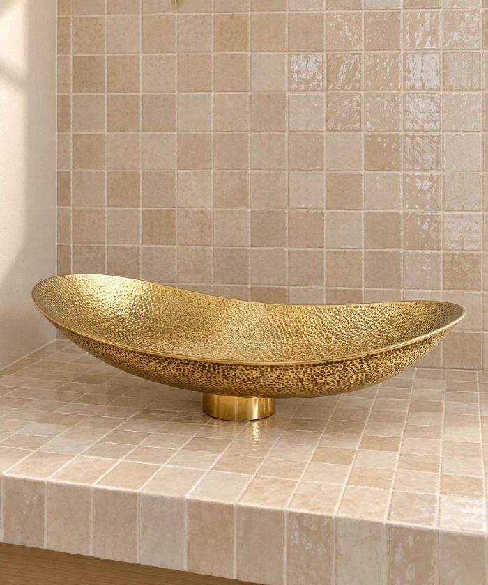 Hand hammered brass vessel sink with elongated oval shape and textured golden finish