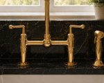 Unlacquered brass bridge faucet with cold water tap and side sprayer in farmhouse kitchen